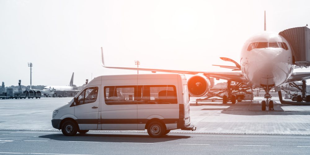 White VIP service van running on airport taxiway with big passenger airplane on background. Business class service at airport. Security intelligence agency hurrying at airfield.